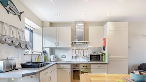 A modern kitchen with white cabinets, stainless steel appliances, and a wooden dining table. - A lovely property in the perfect location, and it has parking too. (Wells-next-the-Sea)