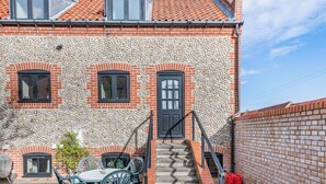 A two-story building with a stone facade, a brick lower section, and a tiled roof. There is a set of stairs leading to a door with a black frame. - A lovely property in the perfect location, and it has parking too. (Wells-next-the-Sea)