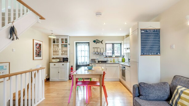 A modern kitchen with white cabinets, a dining area with colorful chairs, and a gray sofa. - A lovely property in the perfect location, and it has parking too. (Wells-next-the-Sea)