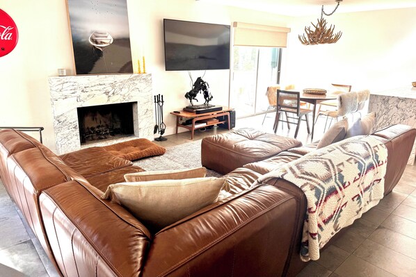 Un salón con un sofá de cuero marrón, una chimenea, un televisor de pantalla plana y un comedor con una mesa y sillas.