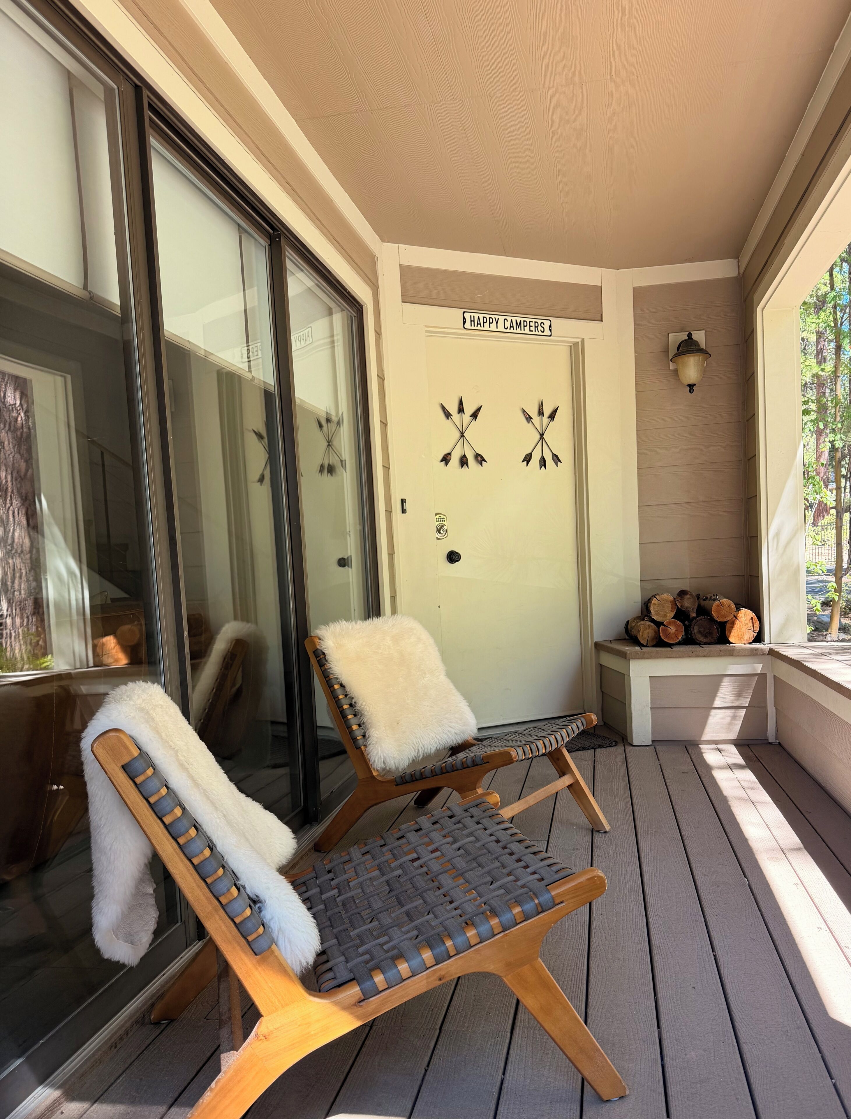 A covered porch with two lounge chairs, a bench, and a door labeled 'HAPPY CAMPERS.'