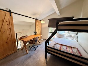 Une chambre avec un lit superposé, un bureau avec une chaise, une lampe et une fenêtre.