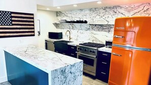 Une cuisine dotée d’un plan de travail en marbre, d’une cuisinière à gaz, d’un four, d’un évier et d’un réfrigérateur orange.