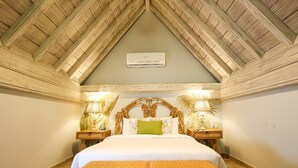 A bedroom with a wooden ceiling, a bed with white bedding, two bedside lamps, and a small table in front of the bed.