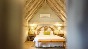 A bedroom with a sloped ceiling, a bed with white bedding, two bedside tables with lamps, and a wooden bench.