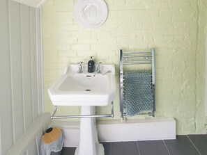 Un baño con un lavabo blanco, un perchero y un espejo en una pared de ladrillo.