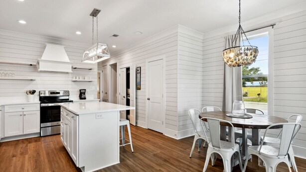 A modern kitchen with white cabinetry, a central island, and a dining area with a round table and white chairs. - New 3 Bedroom Beachfront Rental in downtown Bay St. Louis (Bay St. Louis)