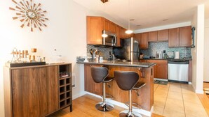 A modern kitchen with wooden cabinets, a central island with bar stools, stainless steel appliances, and a decorative wall clock.