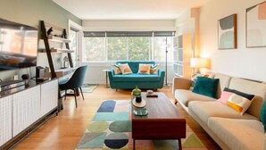 A modern living room with a teal sofa, a wooden coffee table, and a TV on a cabinet.