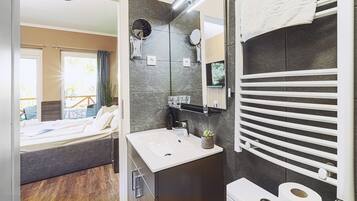 Un baño moderno con un espejo grande, un lavamanos y un inodoro. Hay un perchero sobre el lavamanos y una pequeña maceta en la encimera.