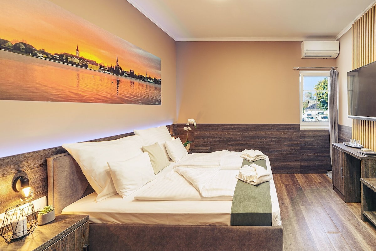 A hotel room with a bed, a TV, a painting, and a window.