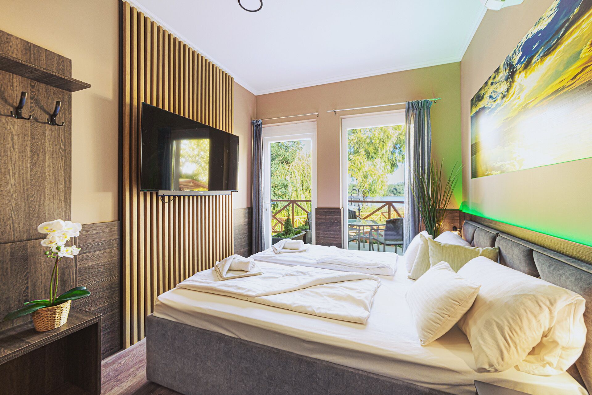 A bedroom with a bed, a TV mounted on the wall, and a balcony with outdoor furniture.