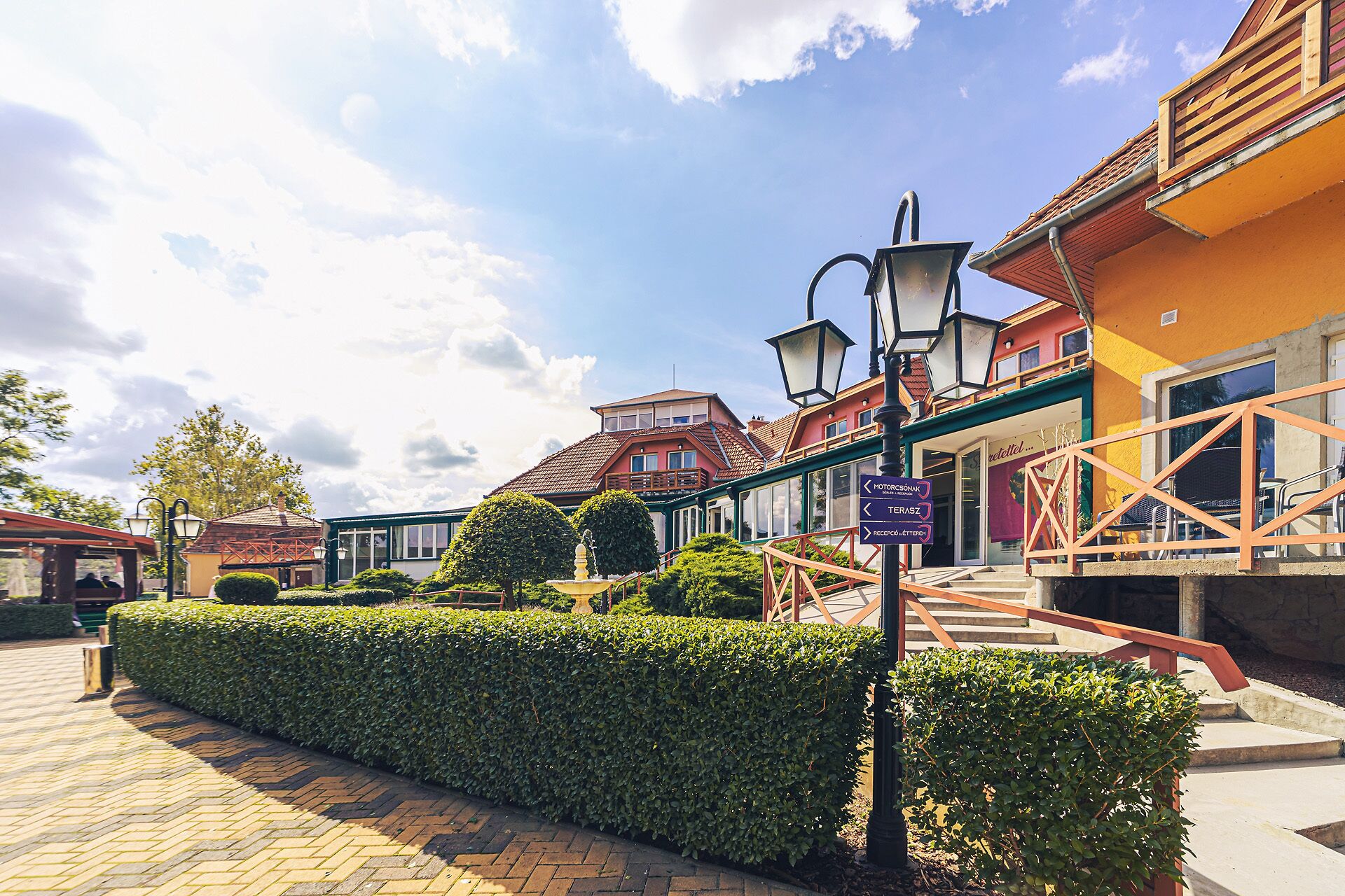 A courtyard with a hedge, a lamp post, and a building with a sign indicating a restaurant.