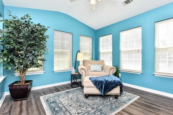 A room with a blue wall, a beige armchair with a blue throw, a large potted plant, and a patterned rug.