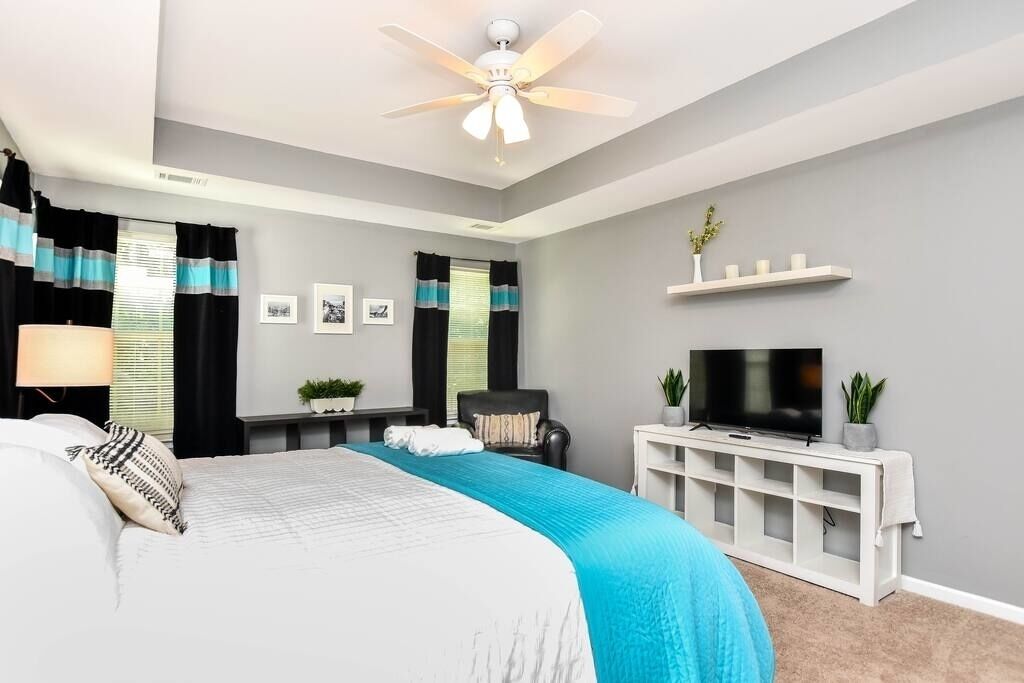 A bedroom with a bed, a ceiling fan, a TV, and a small desk with a chair.
