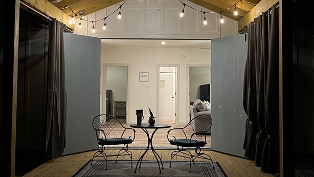 An enclosed patio area with two chairs and a small table, featuring string lights and wooden flooring. - Hidden Bungalow 1 1/2 blocks from the beach (Bay St. Louis)