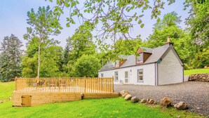 A house with a wooden deck, a stone wall, and a grassy yard. - Dalnaglar Cottage - UK30260 (Glenshee, Cairngorms)