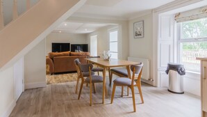 A modern interior with a staircase, a dining area with wooden chairs, a sofa, and a view through a window. - Dalnaglar Cottage - UK30260 (Glenshee, Cairngorms)