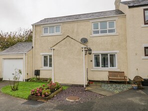 A two-story house with a satellite dish, a garden with flowers, and a bench. - Ravenglass Haven (Ravenglass)