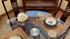Una mesa redonda de vidrio con un mantel tejido, rodeada de sillas con respaldos elaborados.