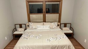 Un dormitorio con una cama grande, dos mesitas de noche, un ventanal con persianas y suelo de madera.