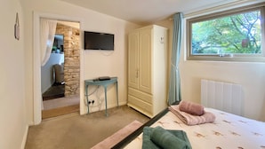 Un dormitorio con cama, televisor montado en la pared, armario y ventana con vistas a árboles.
