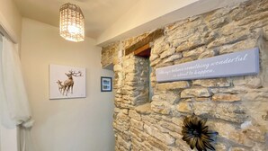 Un pasillo con pared de piedra, un letrero decorativo, un cuadro enmarcado con ciervos y una lámpara colgante.