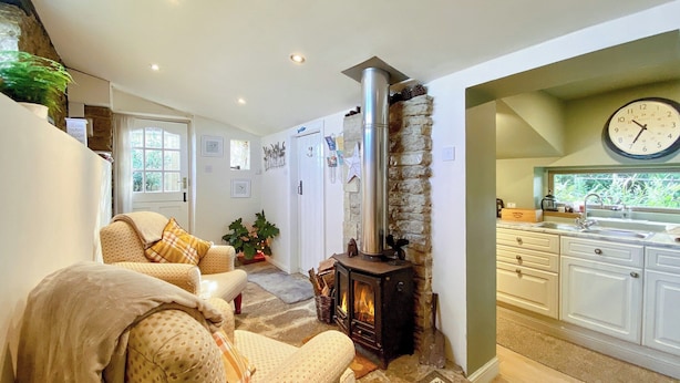 Una sala de estar acogedora con chimenea, una cocina con alacenas blancas y un reloj en la pared.