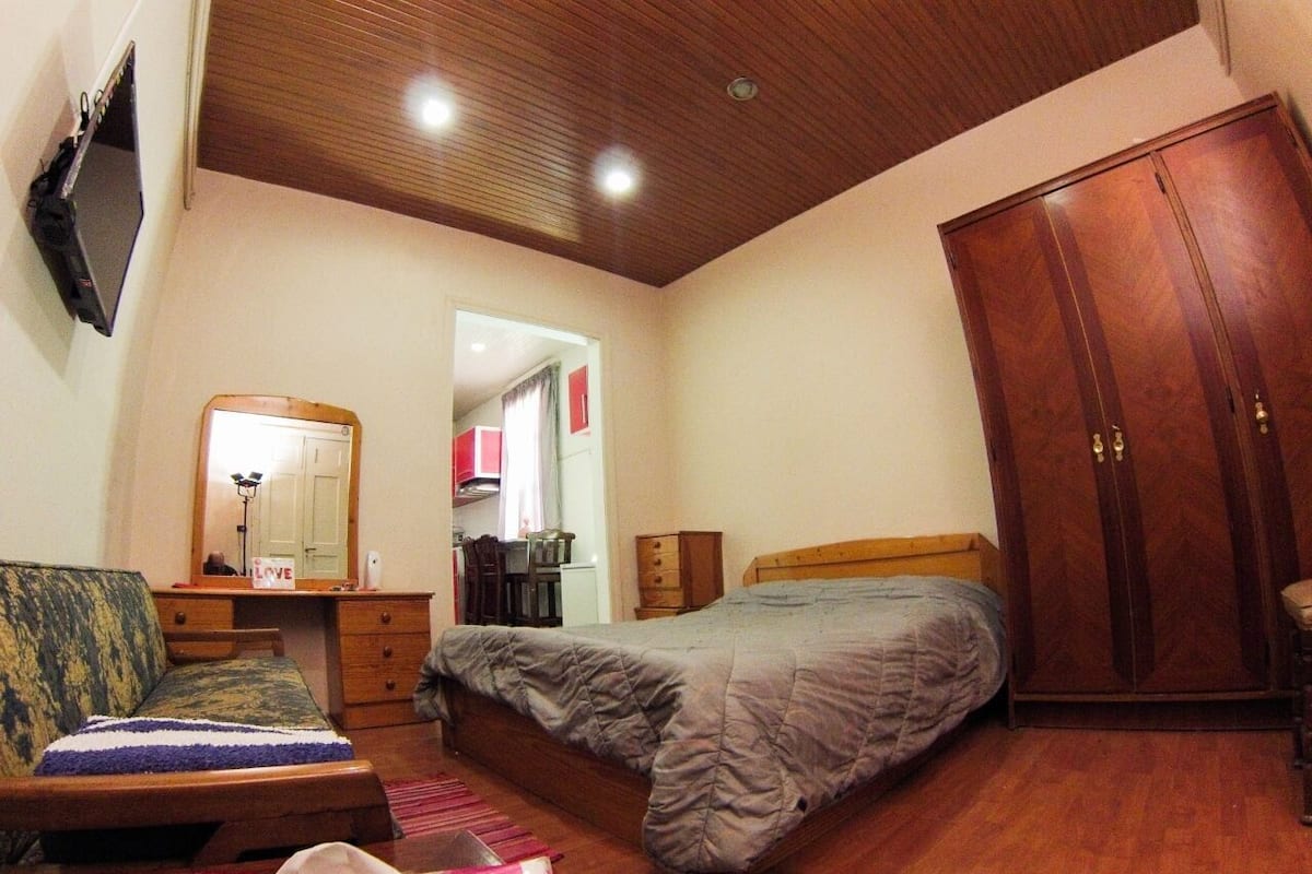 A bedroom with a bed, a wardrobe, a desk, and a chair.