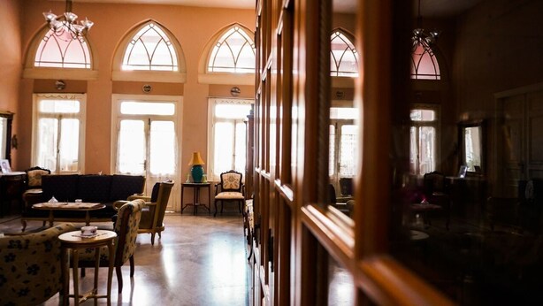 Una habitación amplia con techo alto, grandes ventanas de arco y una zona de estar acogedora con sofá y sillones.