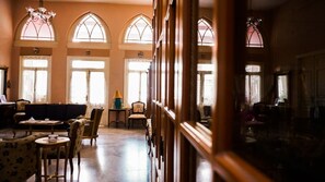 A spacious room with a high ceiling, large arched windows, and a cozy seating area with a sofa and chairs. - Hotel Traboulsi (Zahlé)