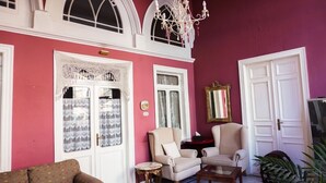 Una habitación con pared rosa, dos puertas blancas, una araña y dos sillones.