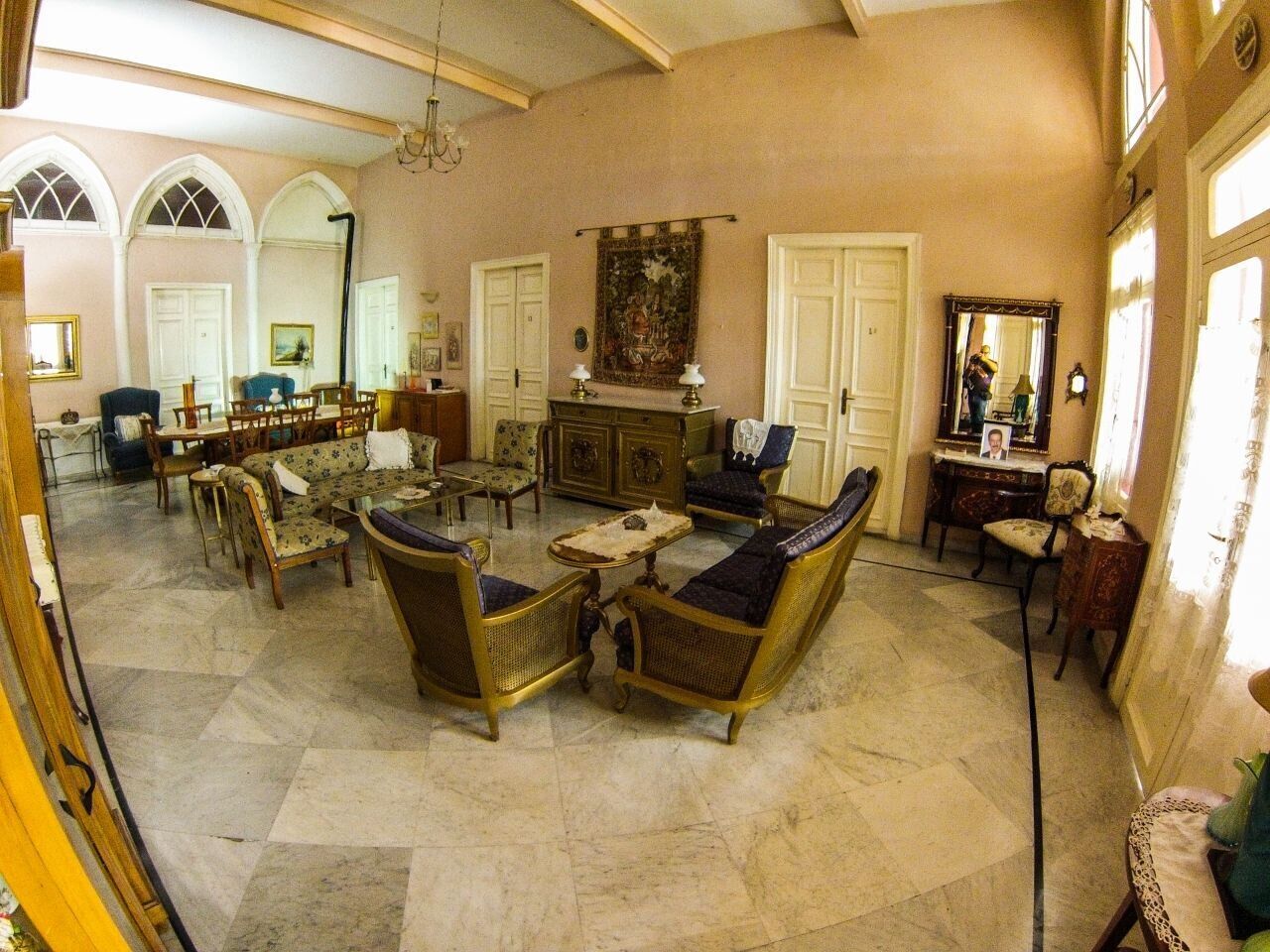 Une pièce spacieuse avec une grande table à manger, plusieurs chaises et un canapé. Un lustre est suspendu au plafond et un grand miroir orne le mur.