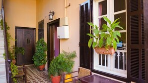Un espacio exterior pequeño y acogedor con suelo de baldosas, una silla de madera, una mesa y varias plantas en macetas.