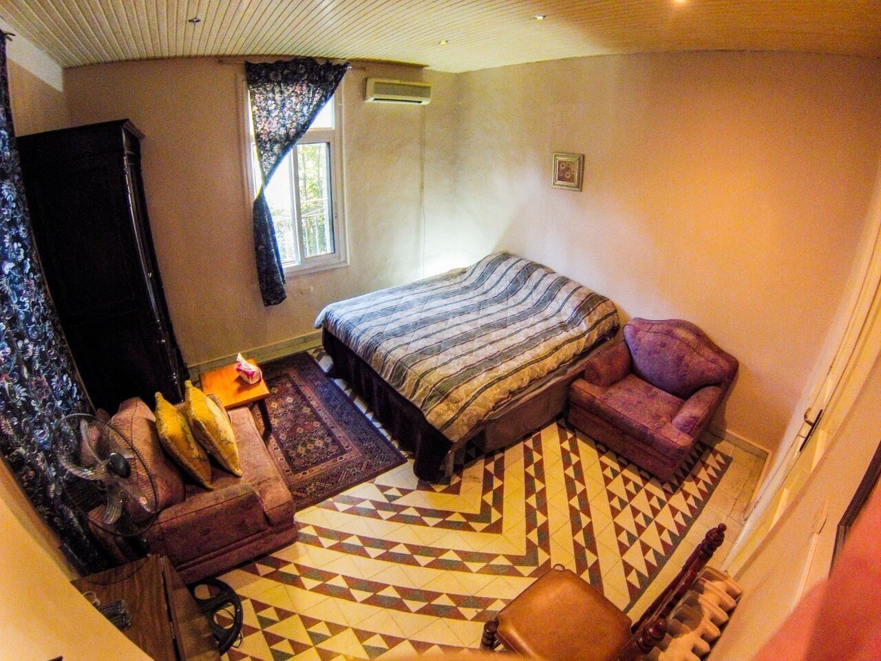 A bedroom with a bed, a sofa, a chair, a fan, and a small table.