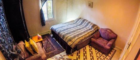 A bedroom with a bed, a sofa, a chair, a fan, and a small table.