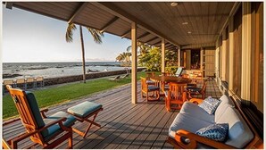 A covered outdoor seating area with a view of the ocean, wooden furniture, and a grassy lawn. - B.I. Kaiakea,  Sleeps 12, Hot Tub, Astounding Oceanfront in Tranquil Puako! (Kamuela)
