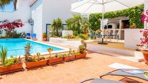 A poolside area with a pool, lounge chairs, and potted plants.