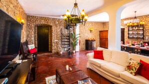 Un salon avec un mur en pierre, une cheminée, un canapé blanc, un téléviseur et un coin repas avec une table dressée pour quatre personnes.