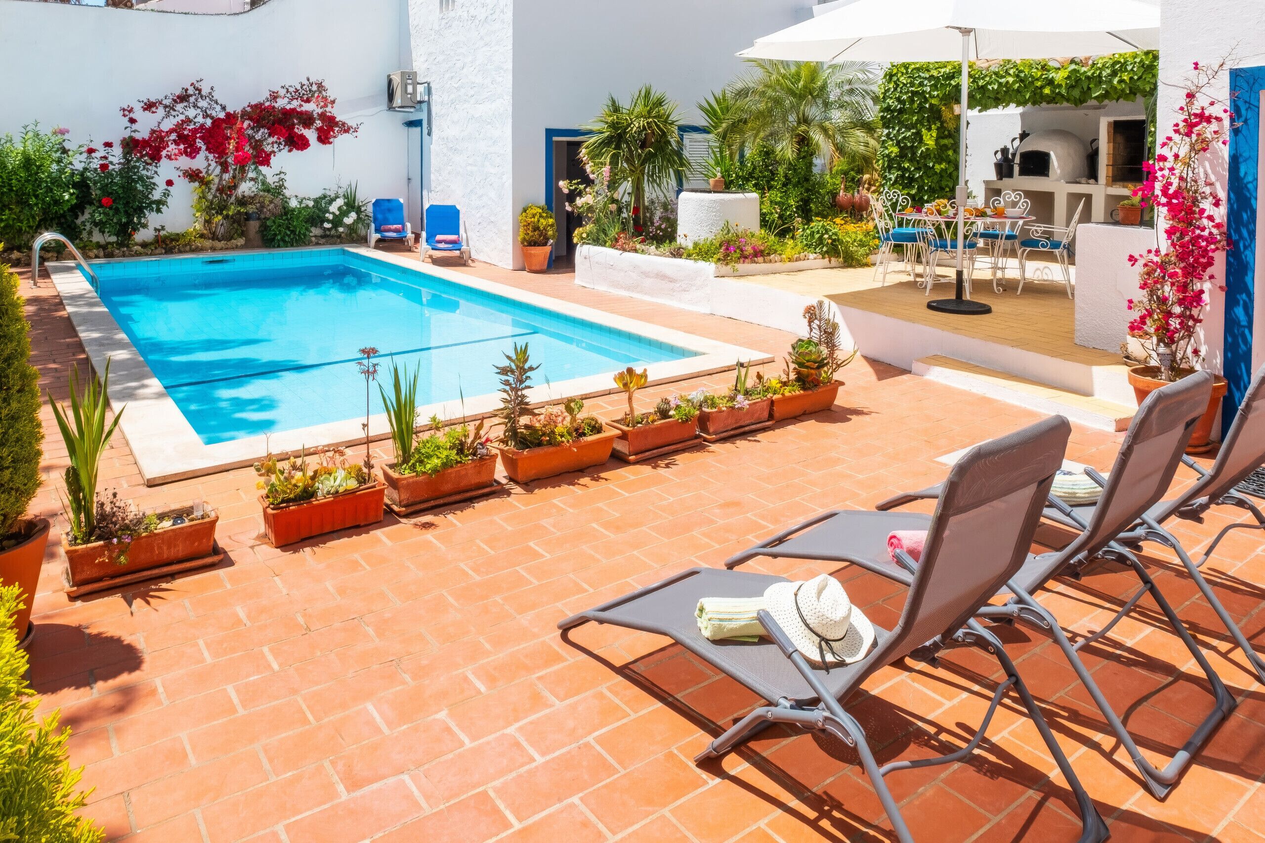 Un espace piscine aménagé avec des chaises longues, des plantes en pot et un barbecue.