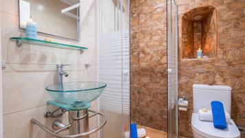 Un baño con lavamanos de vidrio, ducha, pared de piedra y un inodoro con toallas.
