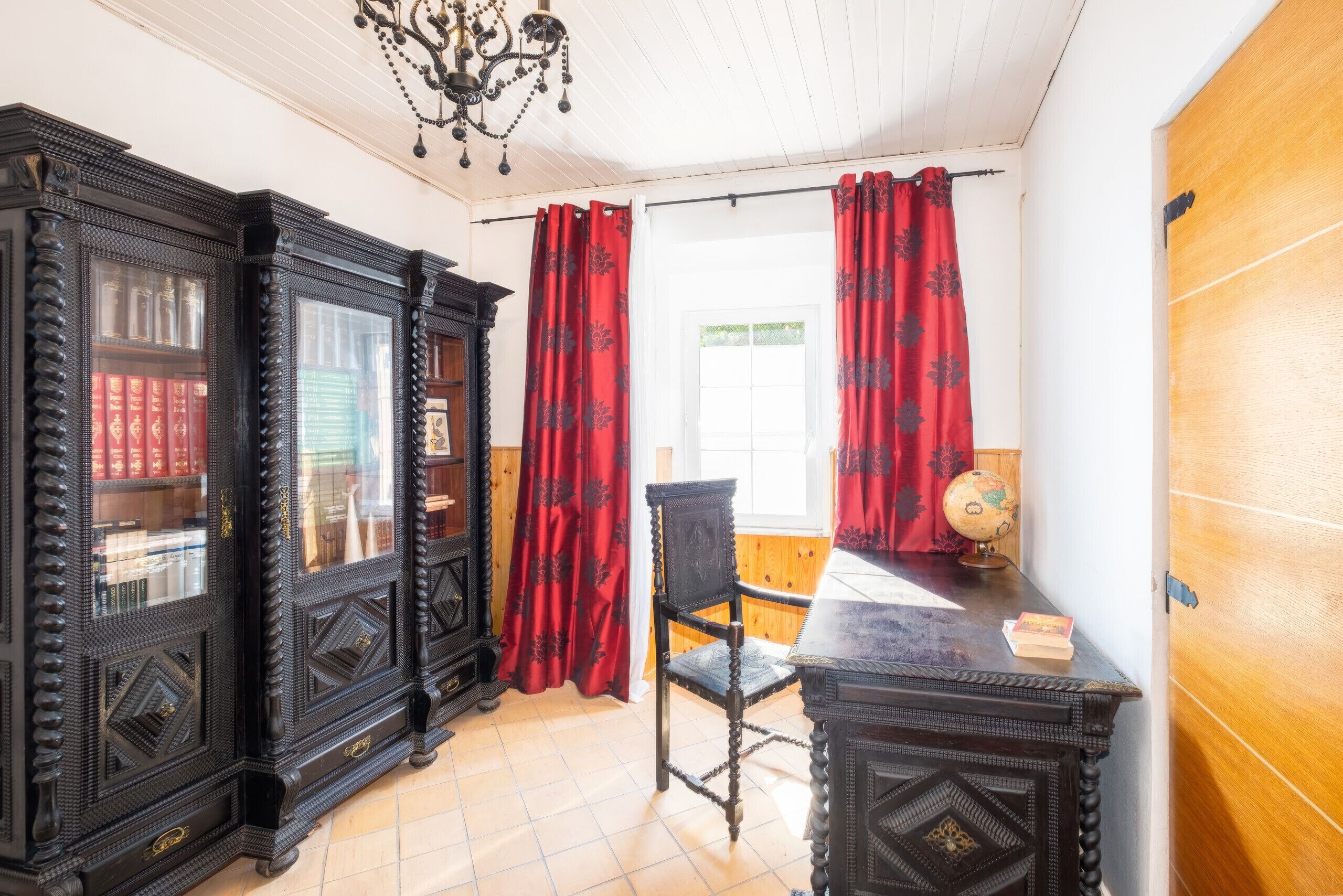 Une pièce avec un bureau en bois, un globe terrestre et une chaise. On y trouve également des étagères remplies de livres et un lustre.