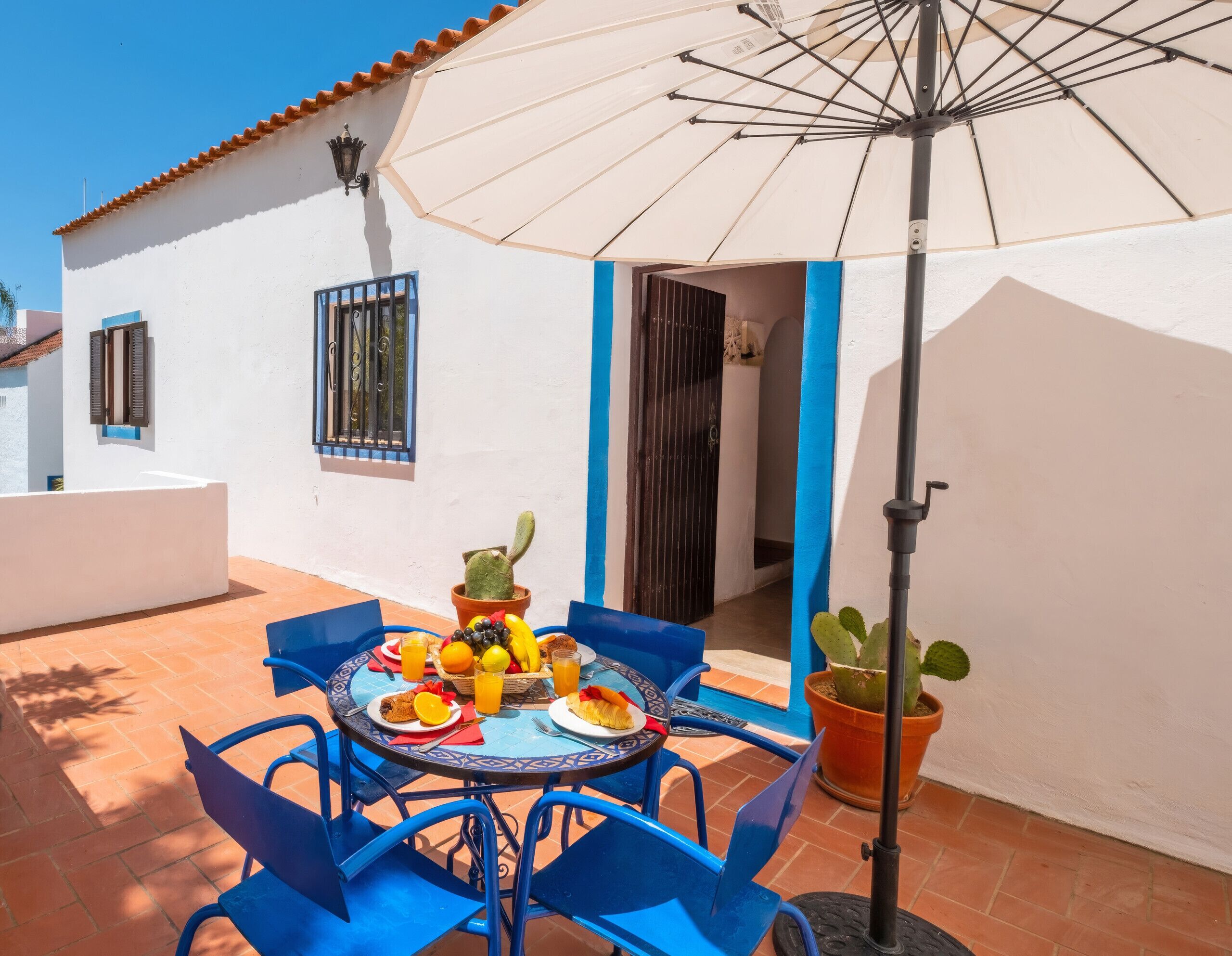 A patio with a table set for breakfast, including fruits and a cactus plant.