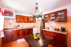 A kitchen with wooden cabinets, a chandelier, a coffee station, and a fruit bowl on the table.