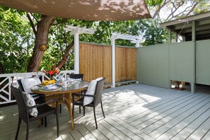 An outdoor patio with a table and chairs, surrounded by a wooden deck and a white fence. - B.I. Plumeria Cottage -Summer Rates! Perfect Couples Getaway in Magical Puako (Kamuela)