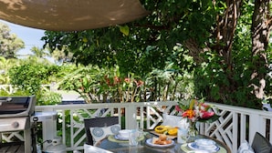 An outdoor dining area with a round table, wicker chairs, and a grill. - B.I. Plumeria Cottage -Summer Rates! Perfect Couples Getaway in Magical Puako (Kamuela)