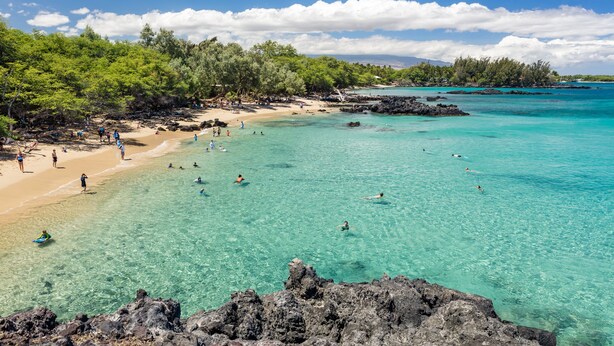 A beach with clear turquoise water, rocky shore, and lush greenery. - B.I. Plumeria Cottage -Summer Rates! Perfect Couples Getaway in Magical Puako (Kamuela)