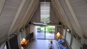 An attic room with a ceiling fan, a TV, a sofa, and a dining table.