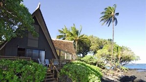 A beachfront property with a wooden house, a staircase leading to the porch, and a view of the ocean.