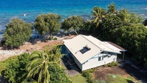 Una casa costera de fachada blanca, rodeada de exuberante vegetación y palmeras, con vista al mar azul cristalino.
